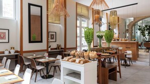 Een modern restaurant met houten meubels, diverse soorten brood op de toonbank en hangende bamboovergoten lampen.