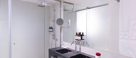 Un baño moderno con ducha envuelta en vidrio, un lavabo negro con espejo y un perchero para toallas.
