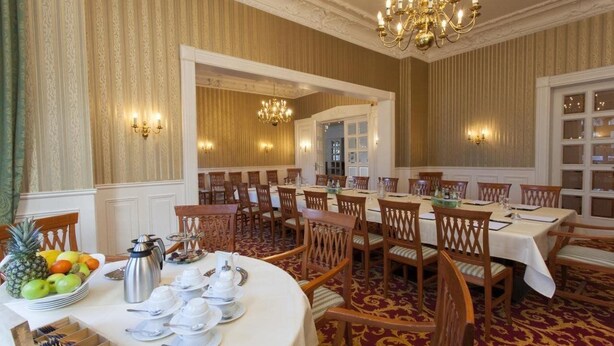 A formal dining room with round tables, wooden chairs, and chandeliers. - Kaiserhof TWO by Centro Basic (Luebeck)