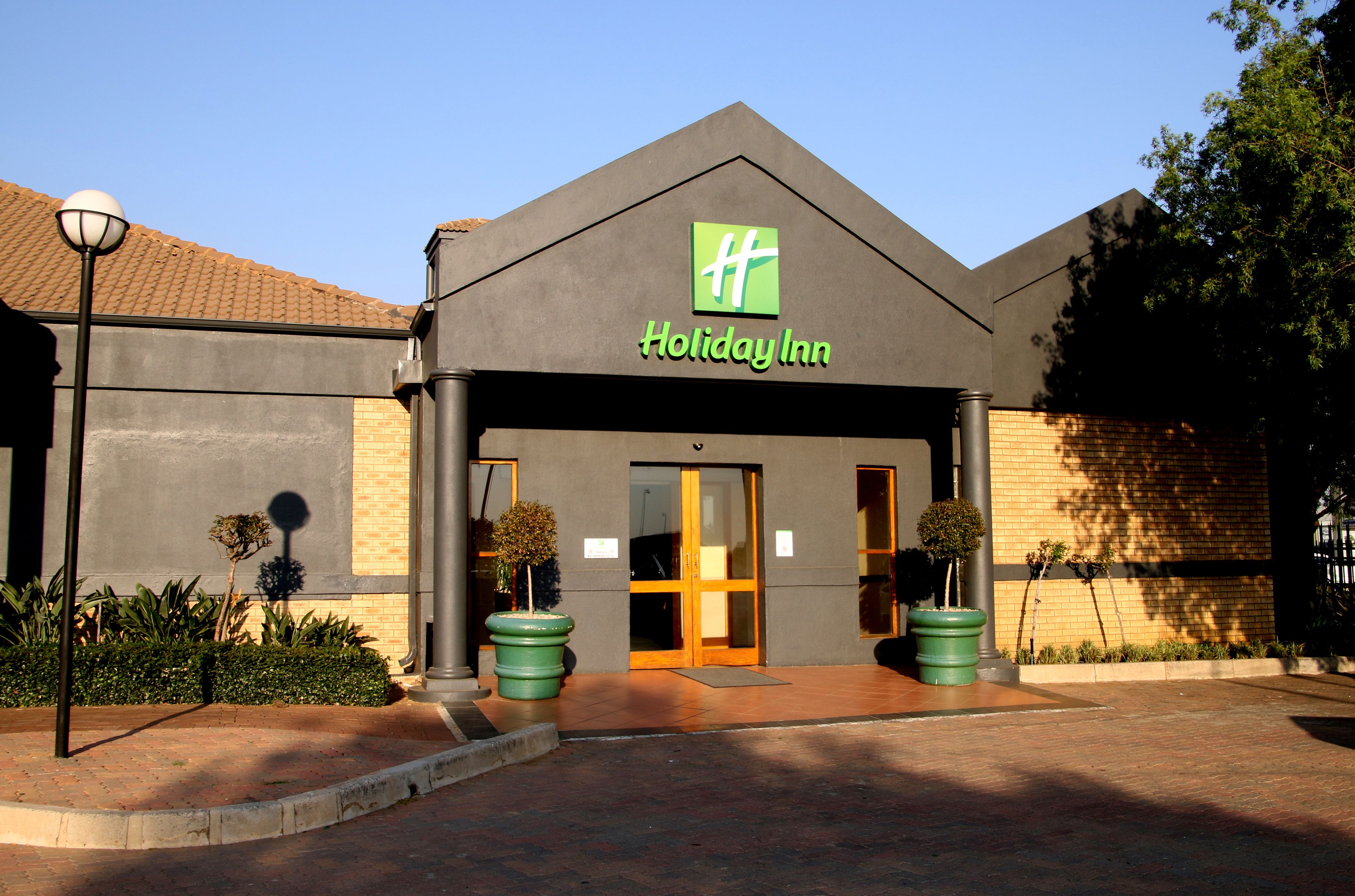 A Holiday Inn hotel with a modern design, featuring a prominent logo, a well-maintained entrance, and potted plants.