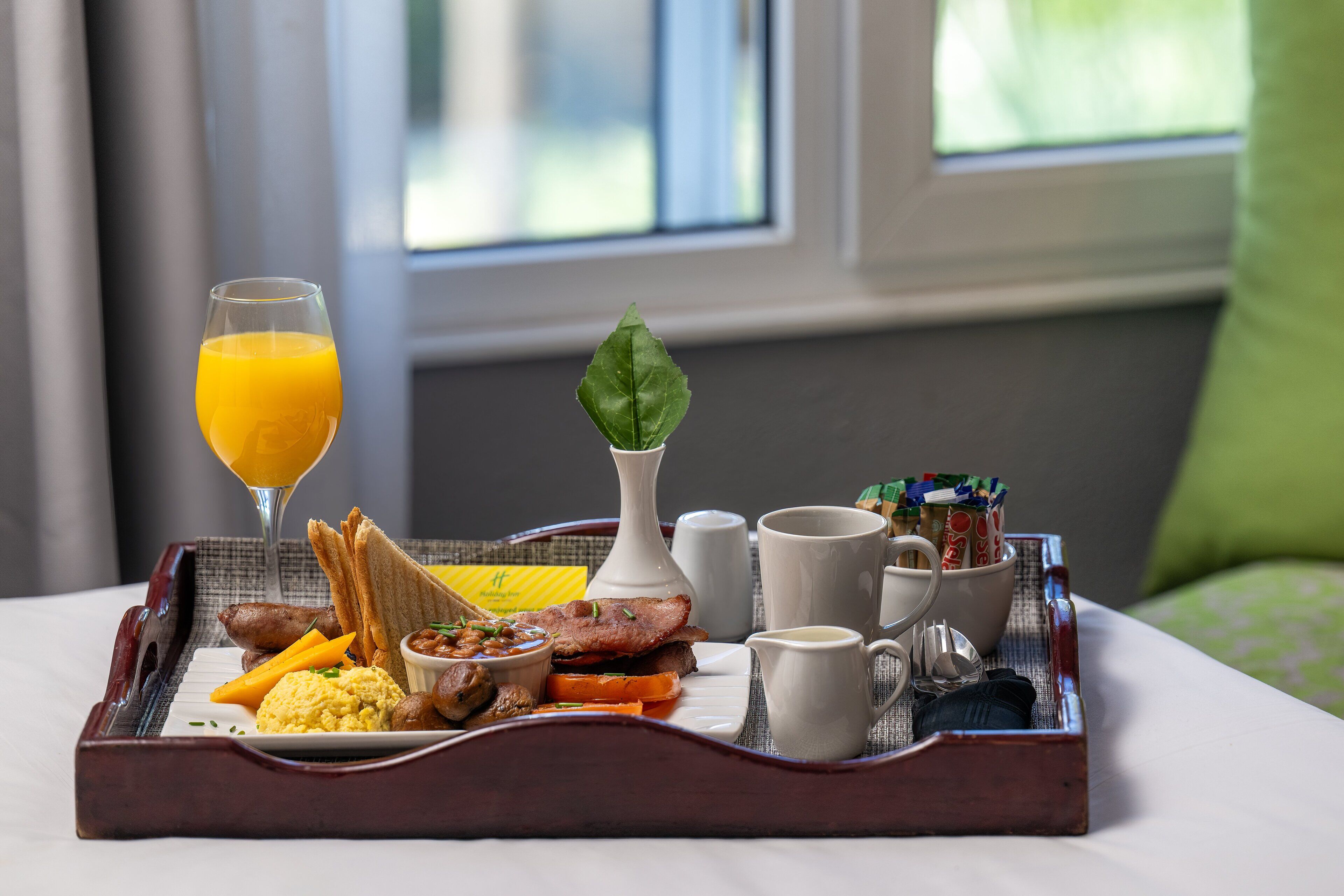 Una bandeja de desayuno con tostadas, huevos revueltos, tocino y un vaso de jugo de naranja sobre una cama en una habitación de hotel.