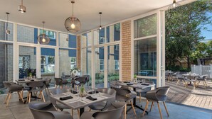 A modern restaurant with large windows, outdoor seating, and contemporary furniture. - Holiday Inn Johannesburg Airport by IHG (Boksburg)