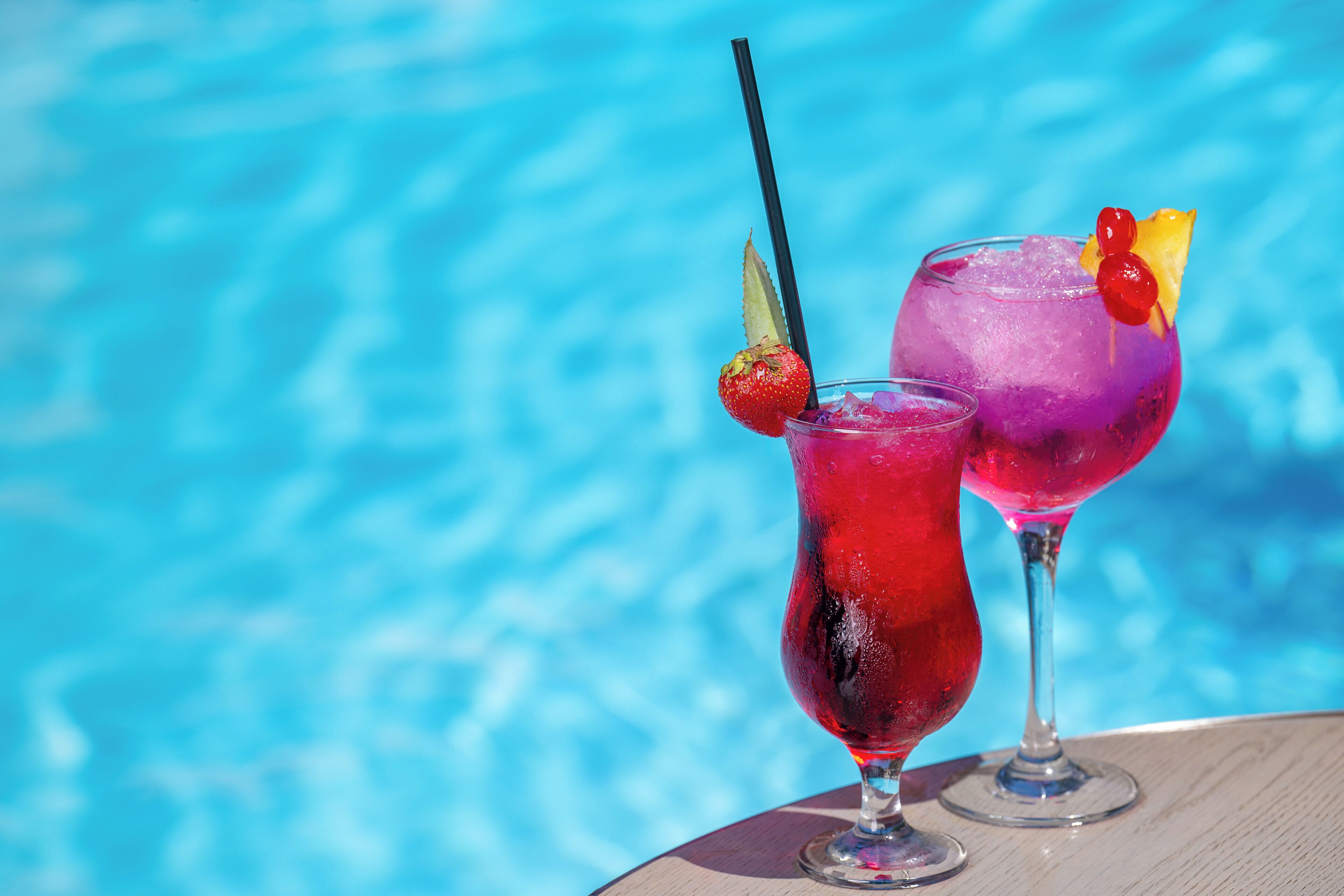 Deux cocktails, décorés de garnitures, avec une piscine en arrière-plan.