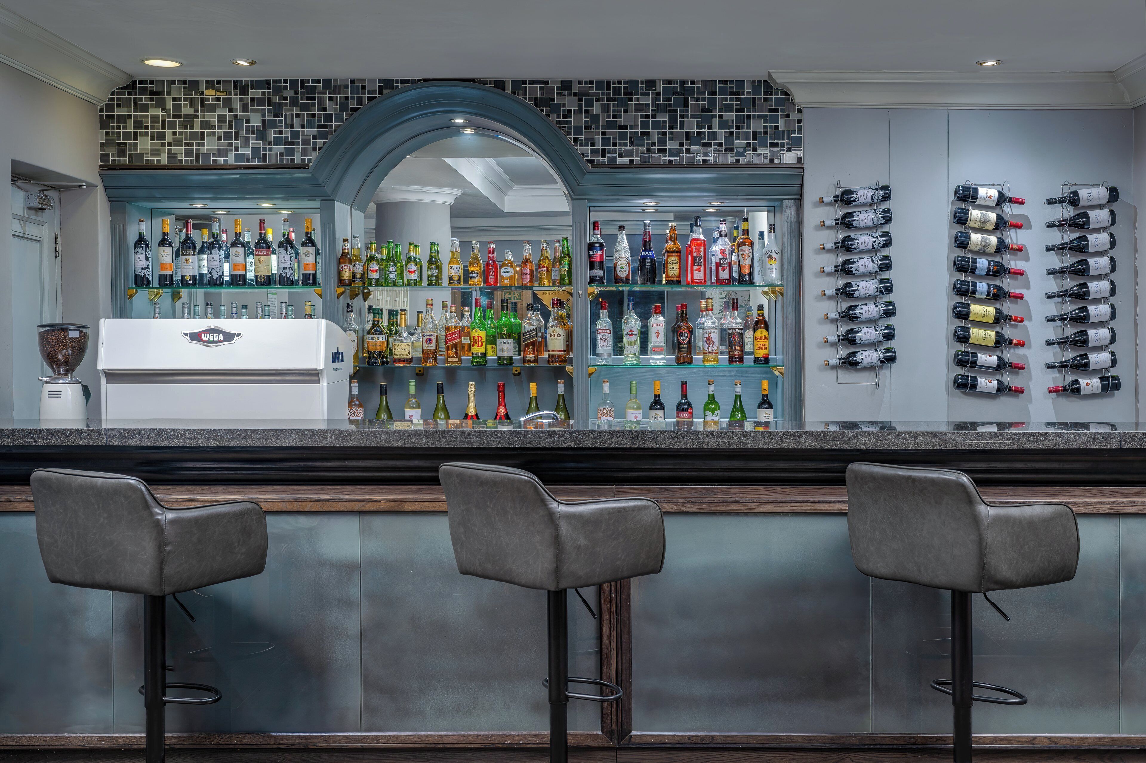 A bar area with a modern design, featuring a wine rack, a variety of liquor bottles, and three bar stools.