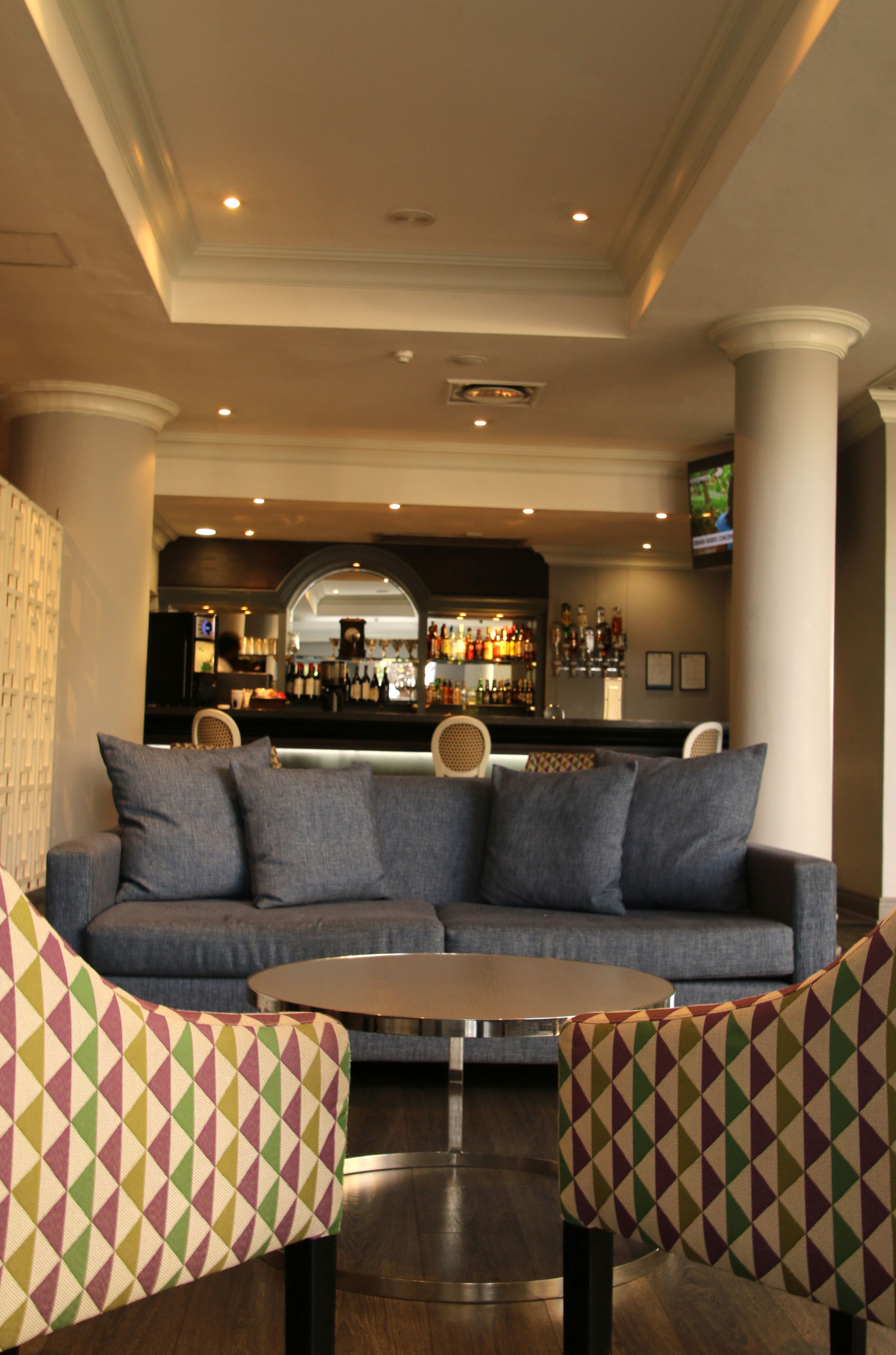A bar area with a sofa and chairs, a round table, and a bar counter with bottles and glasses.