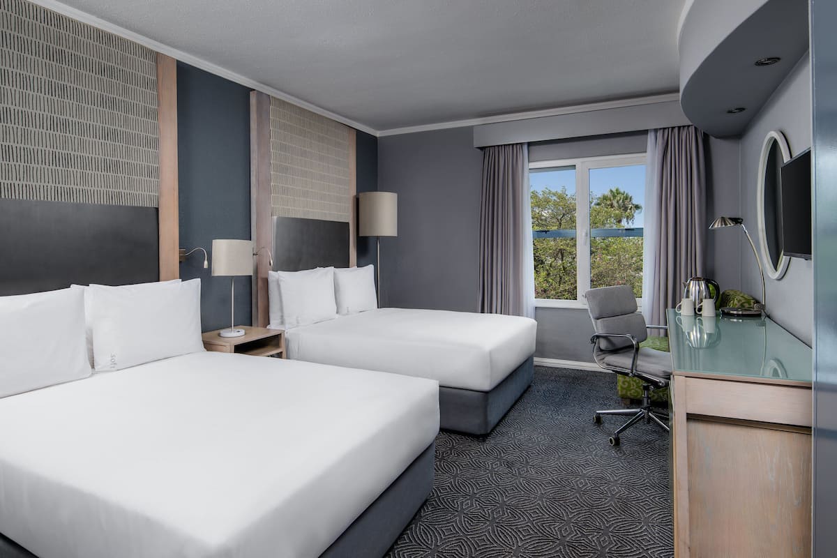 A hotel room with two beds, a desk, a chair, a TV, and a window with curtains.