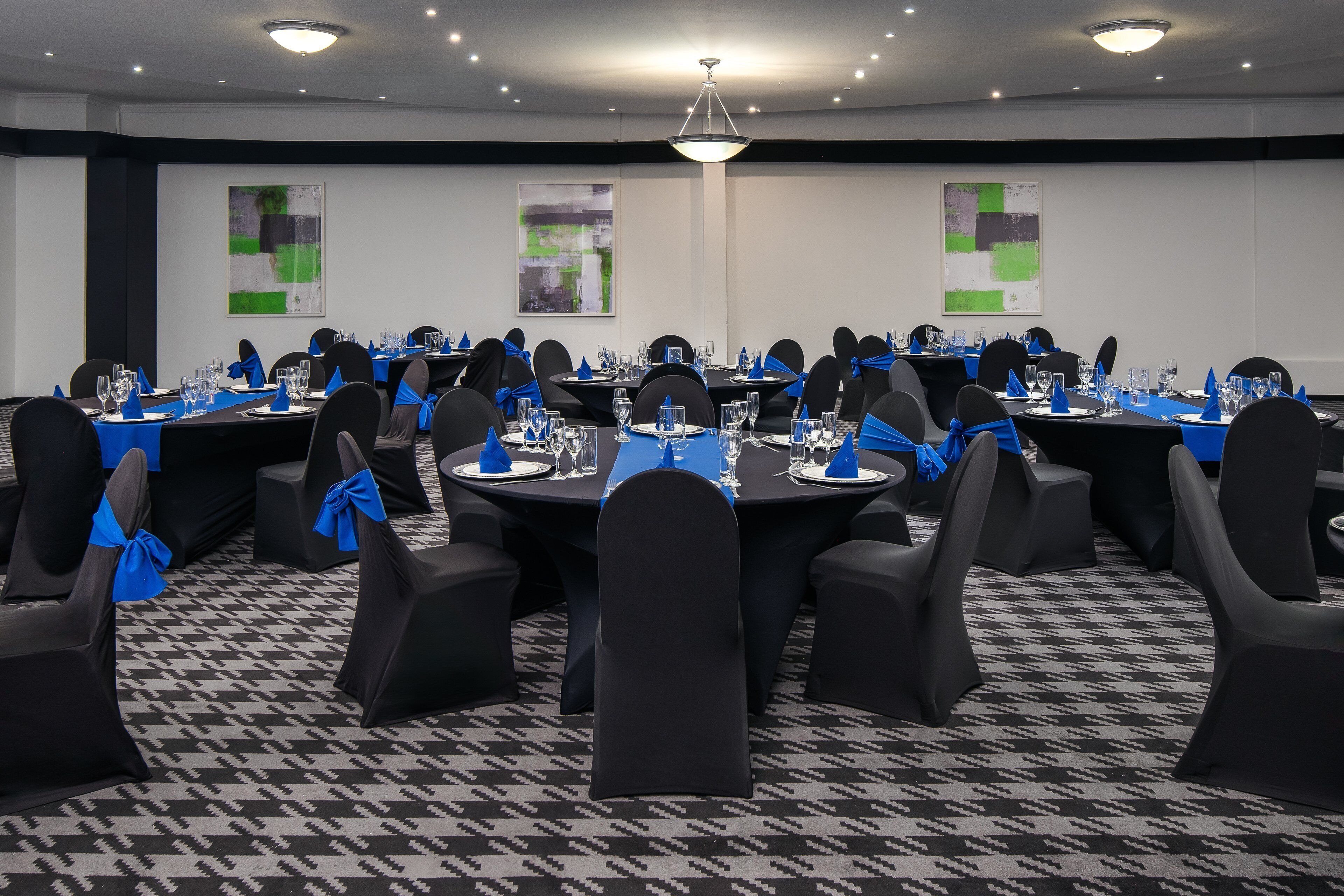 Un salón de conferencias con mesas redondas, sillas negras y fajines azules.