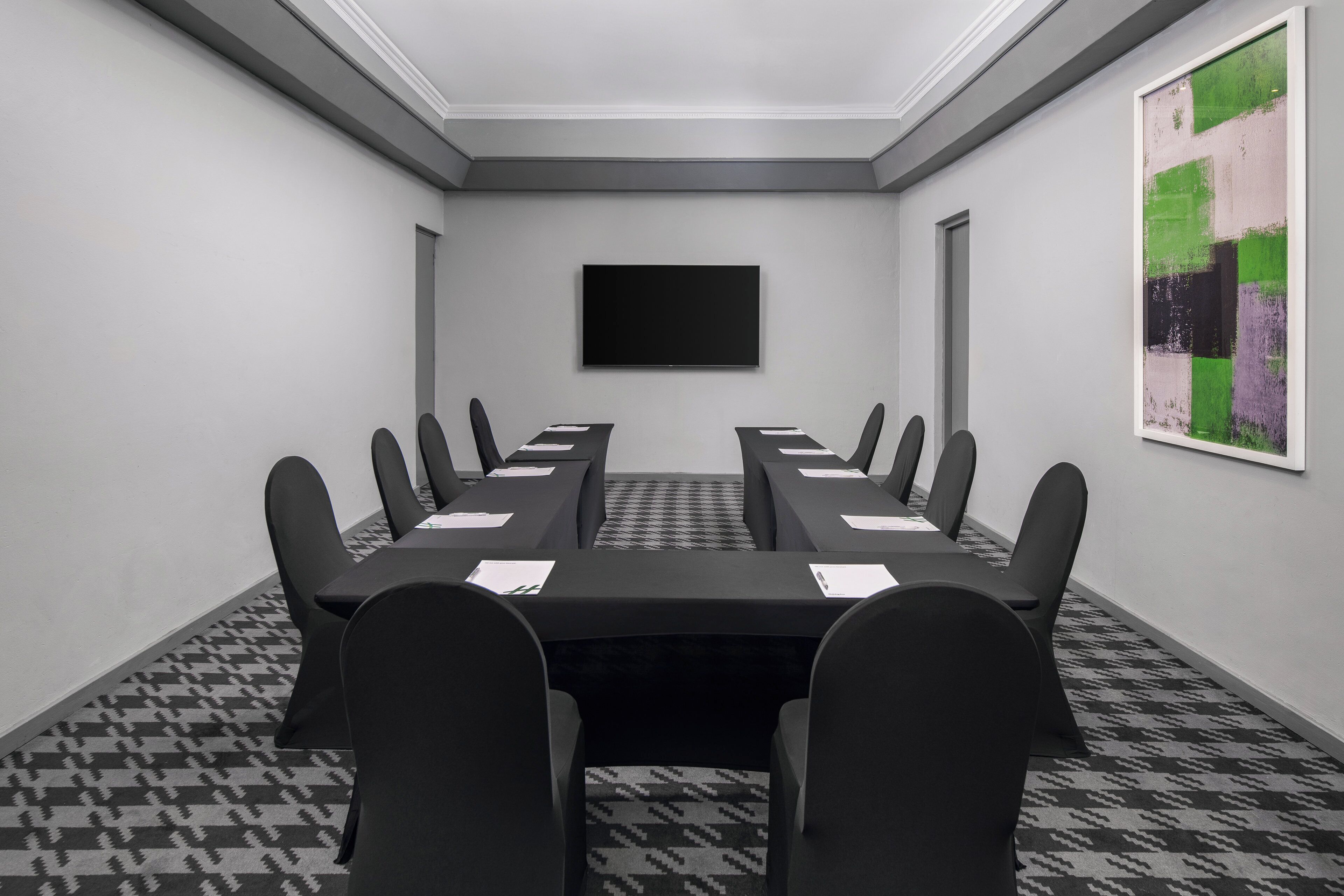 Une salle de conférence avec une longue table, des chaises, un téléviseur à écran plat et une moquette à motifs.