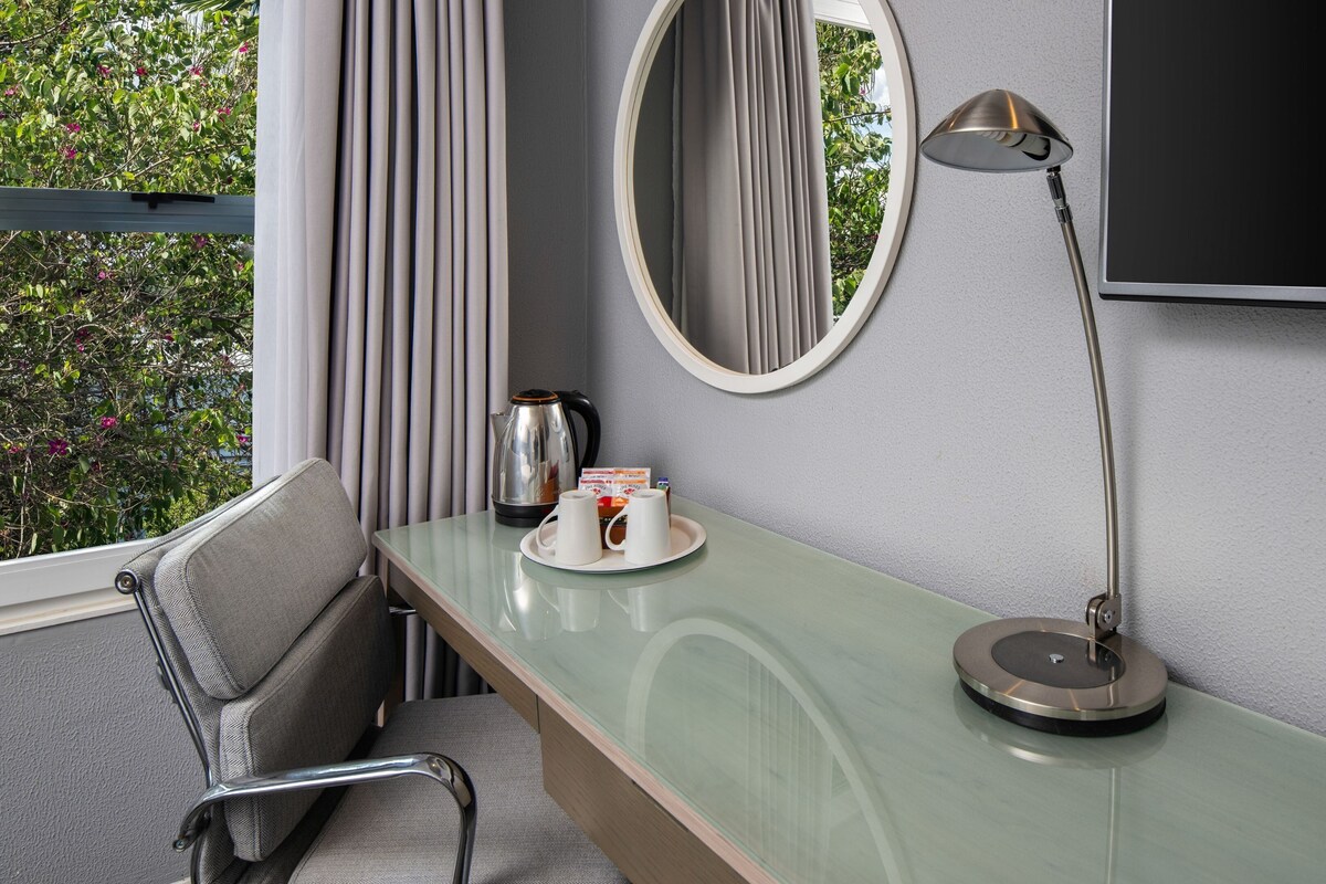 A hotel room with a bed, a desk with a lamp, a TV, and a window with curtains.