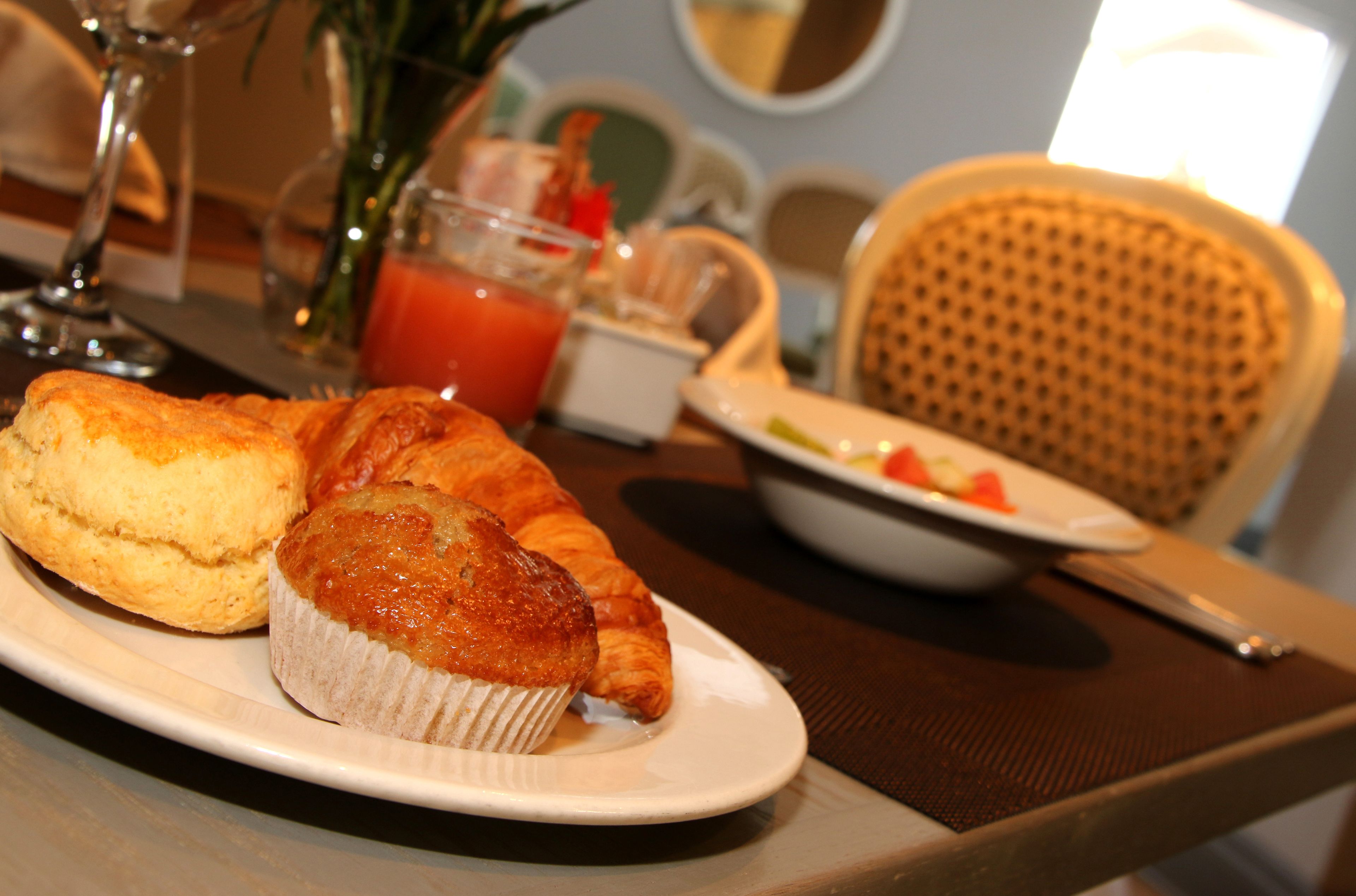 A breakfast setting with a plate of muffins and croissants, a glass of juice, and a bowl of fruit on a table.