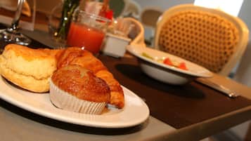 A breakfast setting with a plate of muffins and croissants, a glass of juice, and a bowl of fruit on a table.