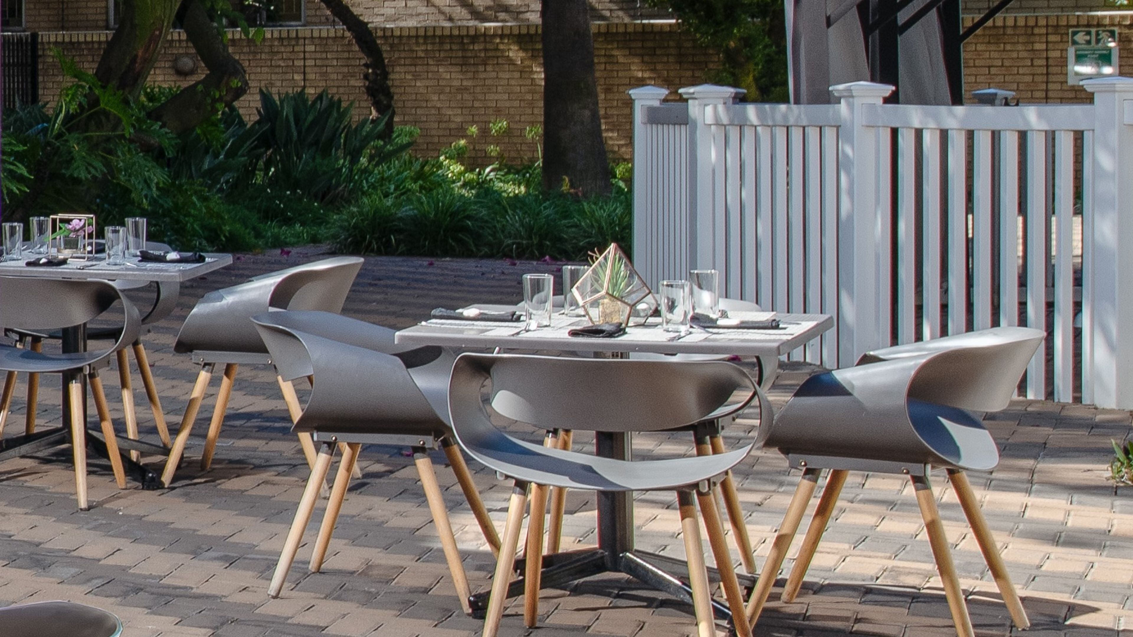 Un espace extérieur aménagé pour les repas, avec des tables et des chaises, entouré d’un mur de briques et de verdure.