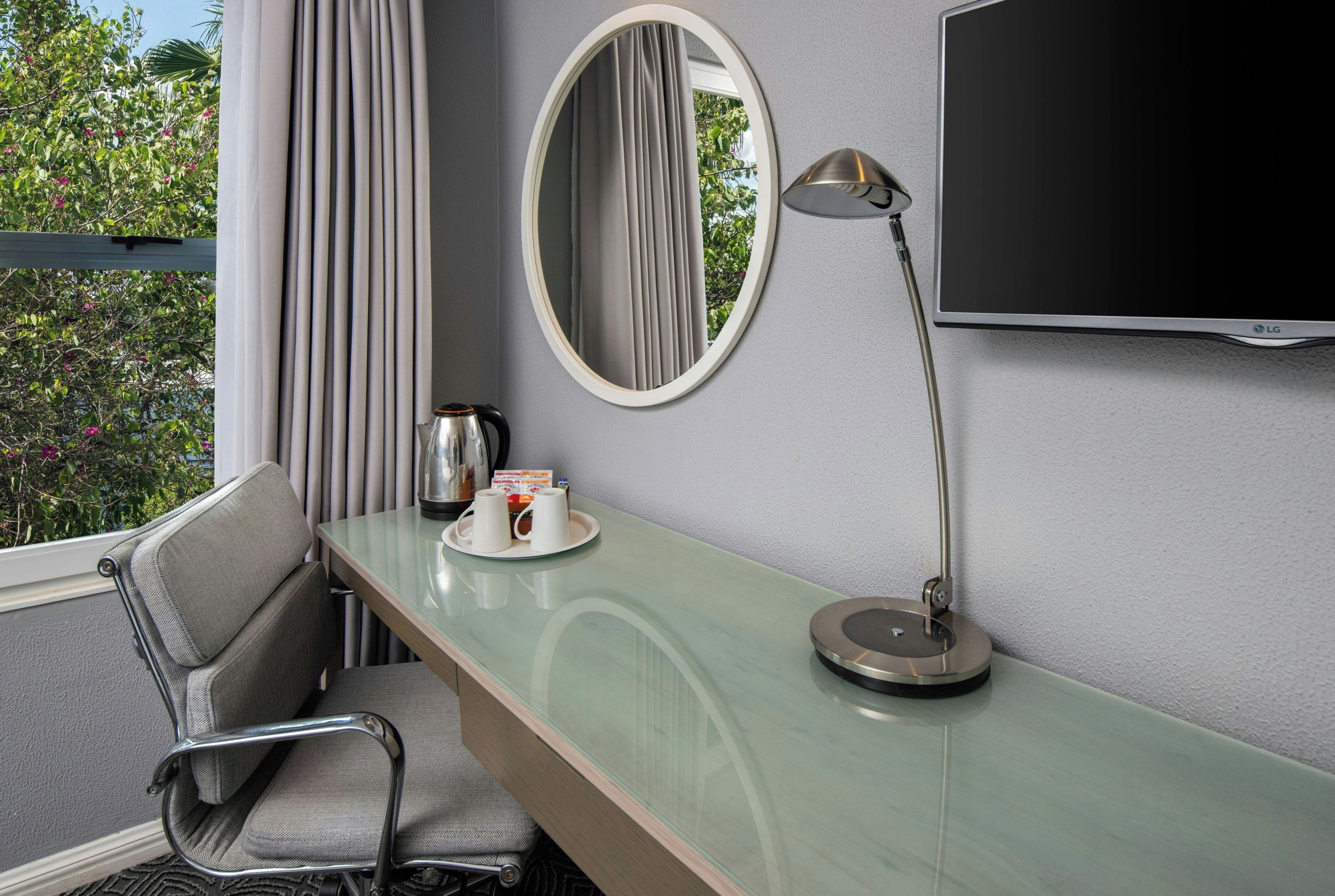 A hotel room with a bed, a desk with a lamp, a television, a chair, and a window with curtains.