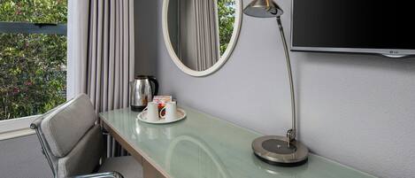 A hotel room with a bed, a desk with a lamp, a television, a chair, and a window with curtains.