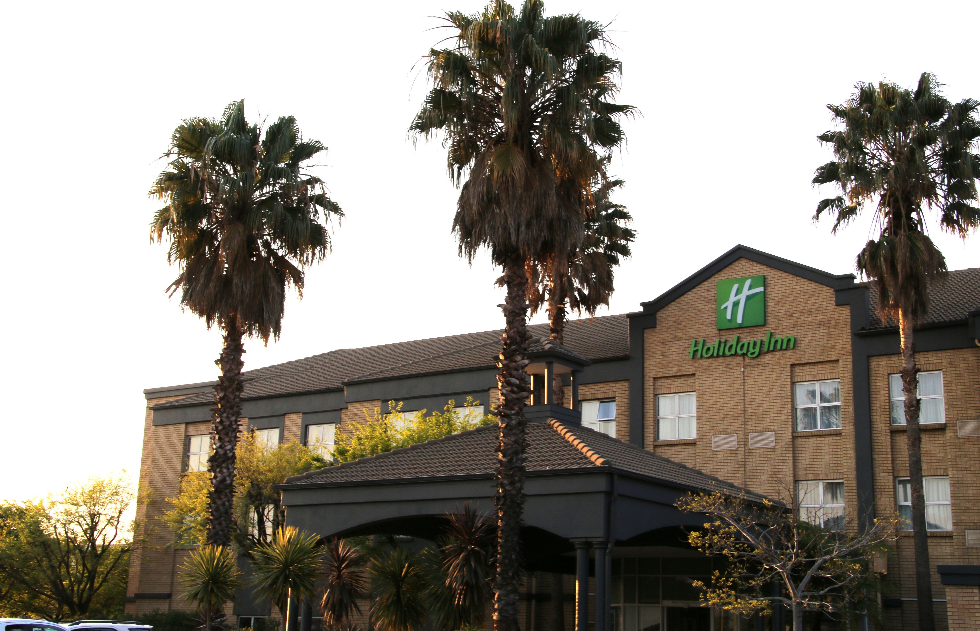 A Holiday Inn hotel with a brick facade, palm trees, and a covered entrance.