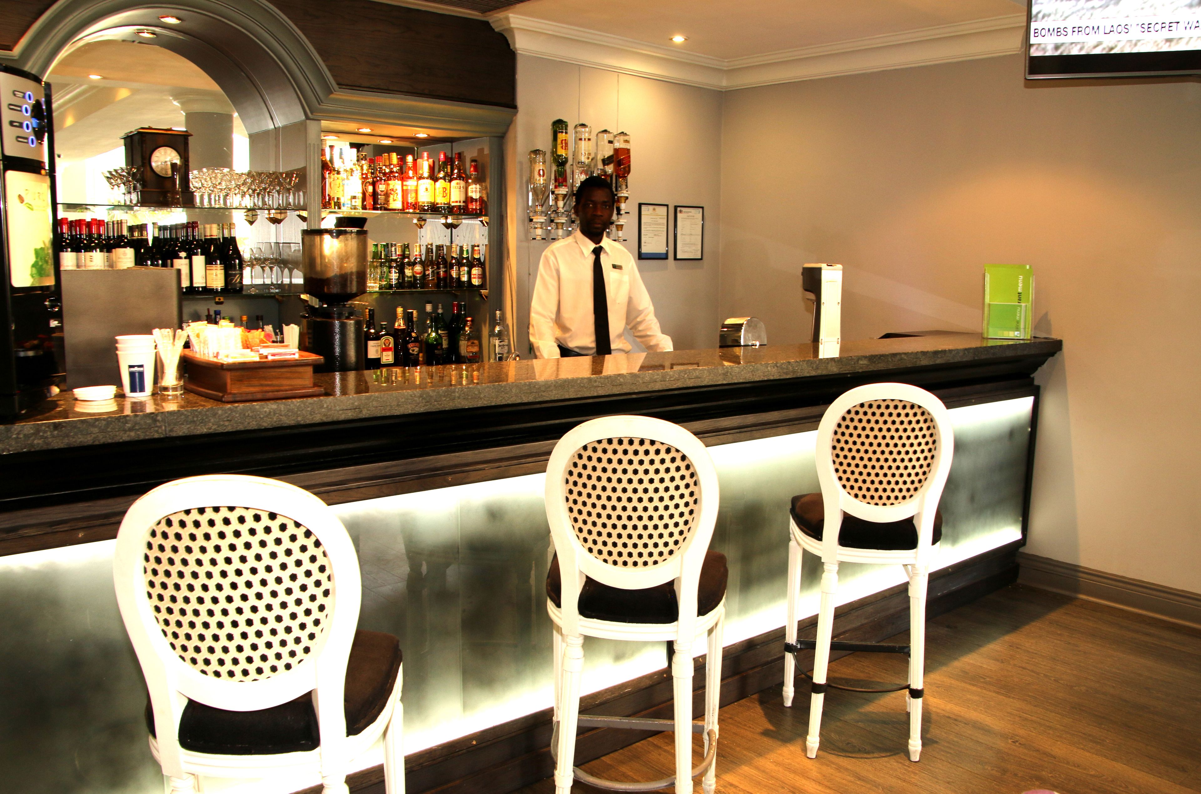 A bar area with a bartender, bar counter, and three white bar stools.