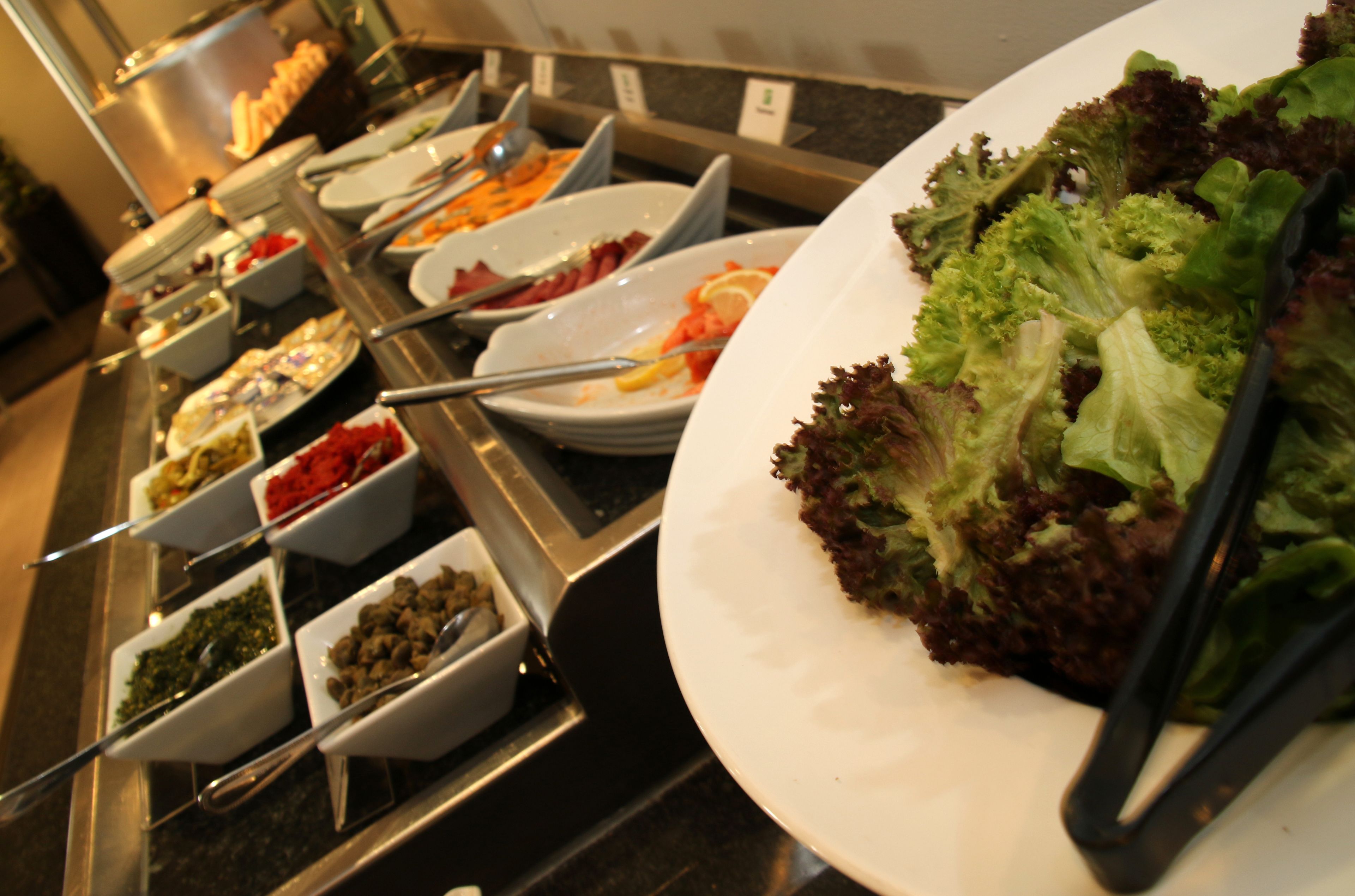 A buffet with various dishes and a large plate of salad.