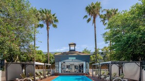 A swimming pool with lounge chairs and a gymnasium in the background. - Holiday Inn Johannesburg Airport by IHG (Boksburg)