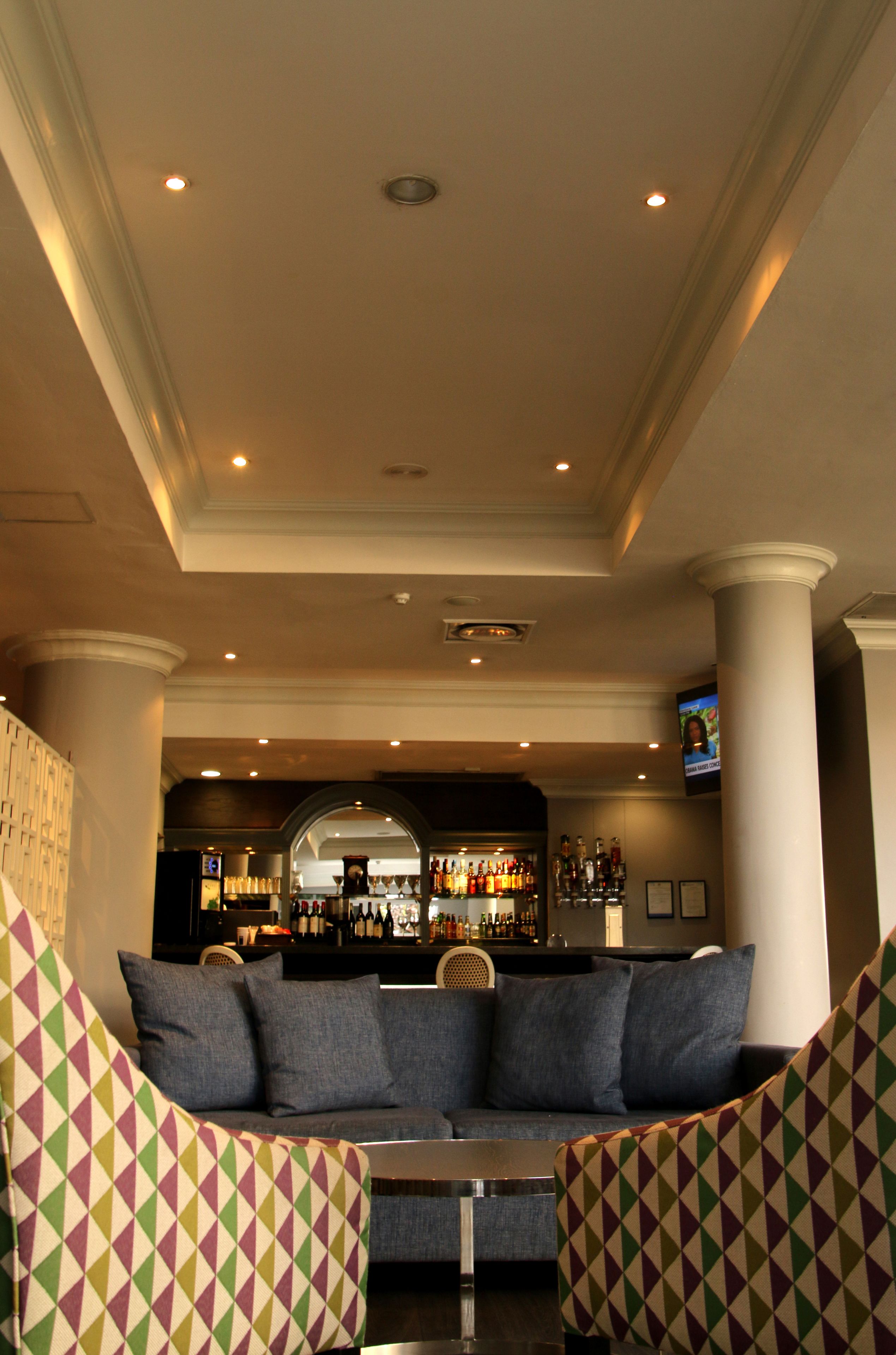 A bar area with a sofa and armchairs, a television, and a bar stocked with bottles.