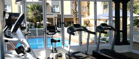 Un gimnasio con cintas de correr, elípticas y una piscina visibles a través de amplios ventanales.