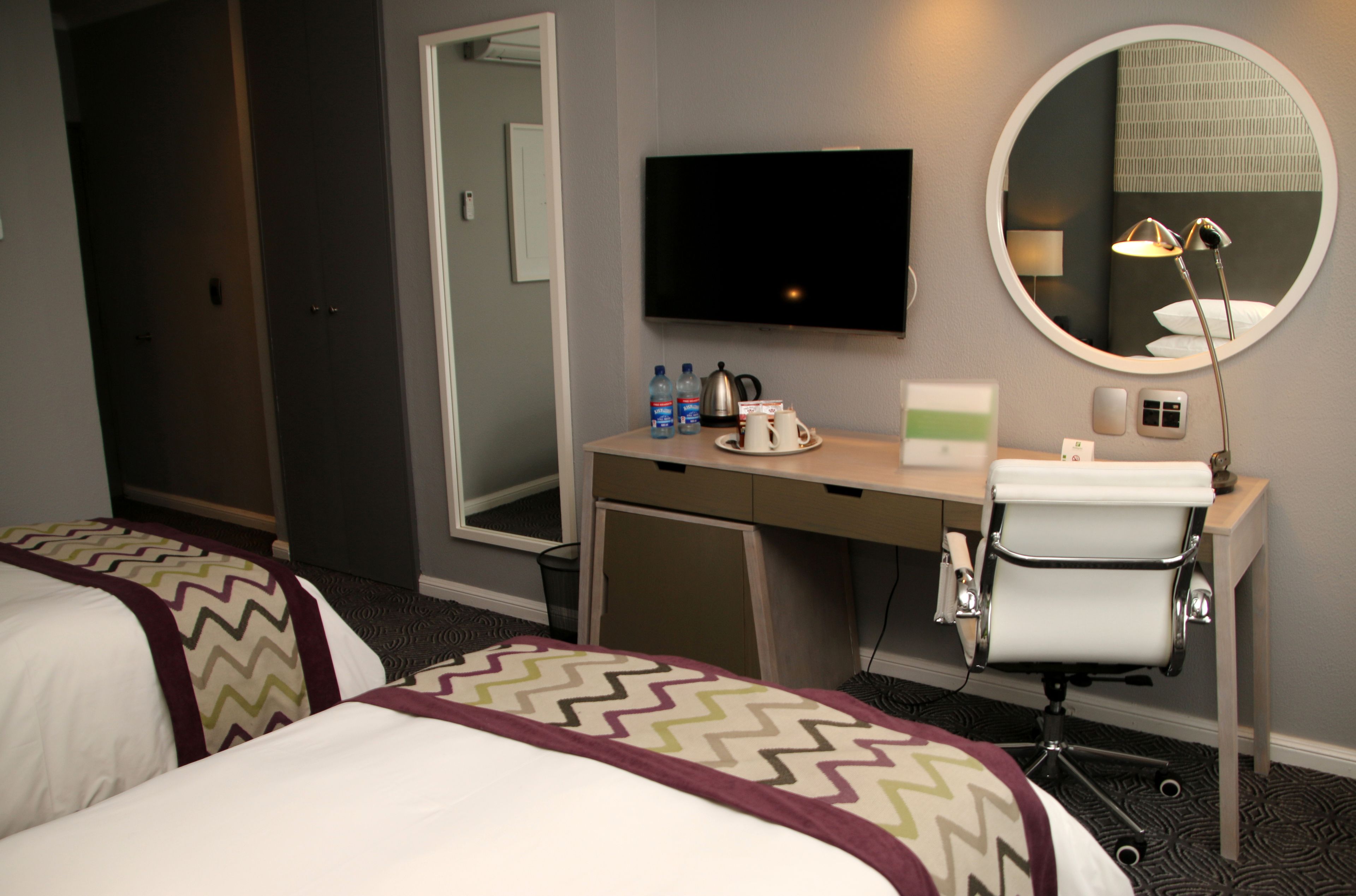 A hotel room with two beds, a desk with a mirror, a television, and a chair.