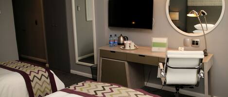 Habitación de hotel con dos camas, un escritorio con espejo, televisión y una silla.