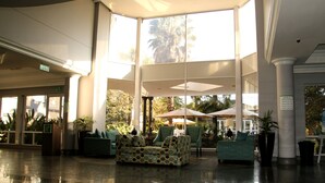 A spacious lobby with a high ceiling, large windows, and a seating area with patterned sofas and armchairs. - Holiday Inn Johannesburg Airport by IHG (Boksburg)