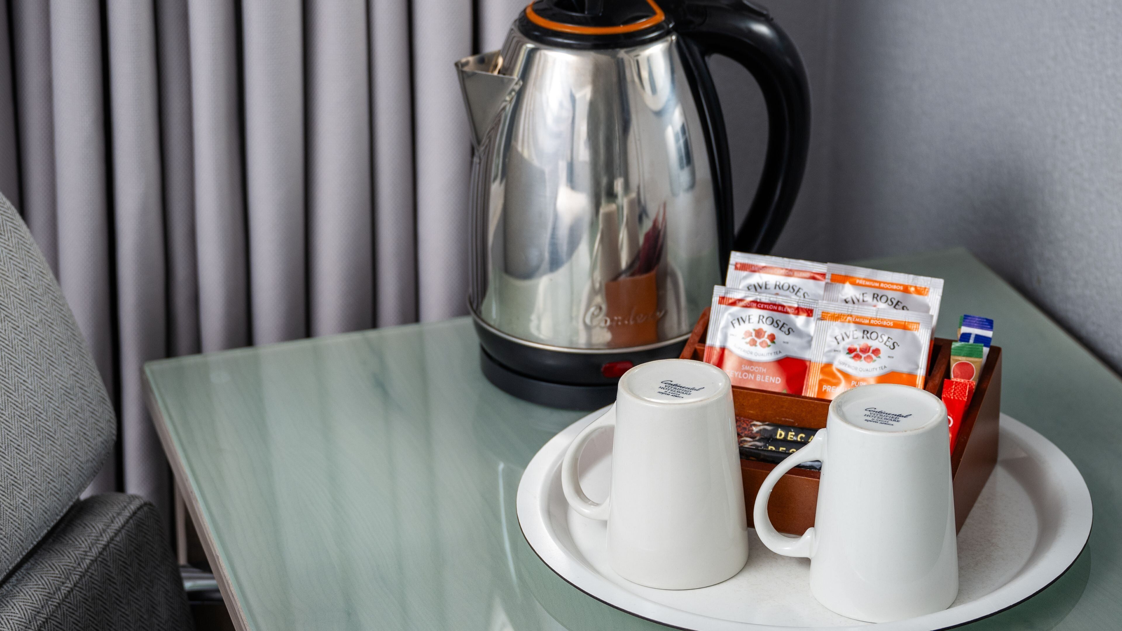 A table with a coffee pot, tea packets, and two white cups on a tray.