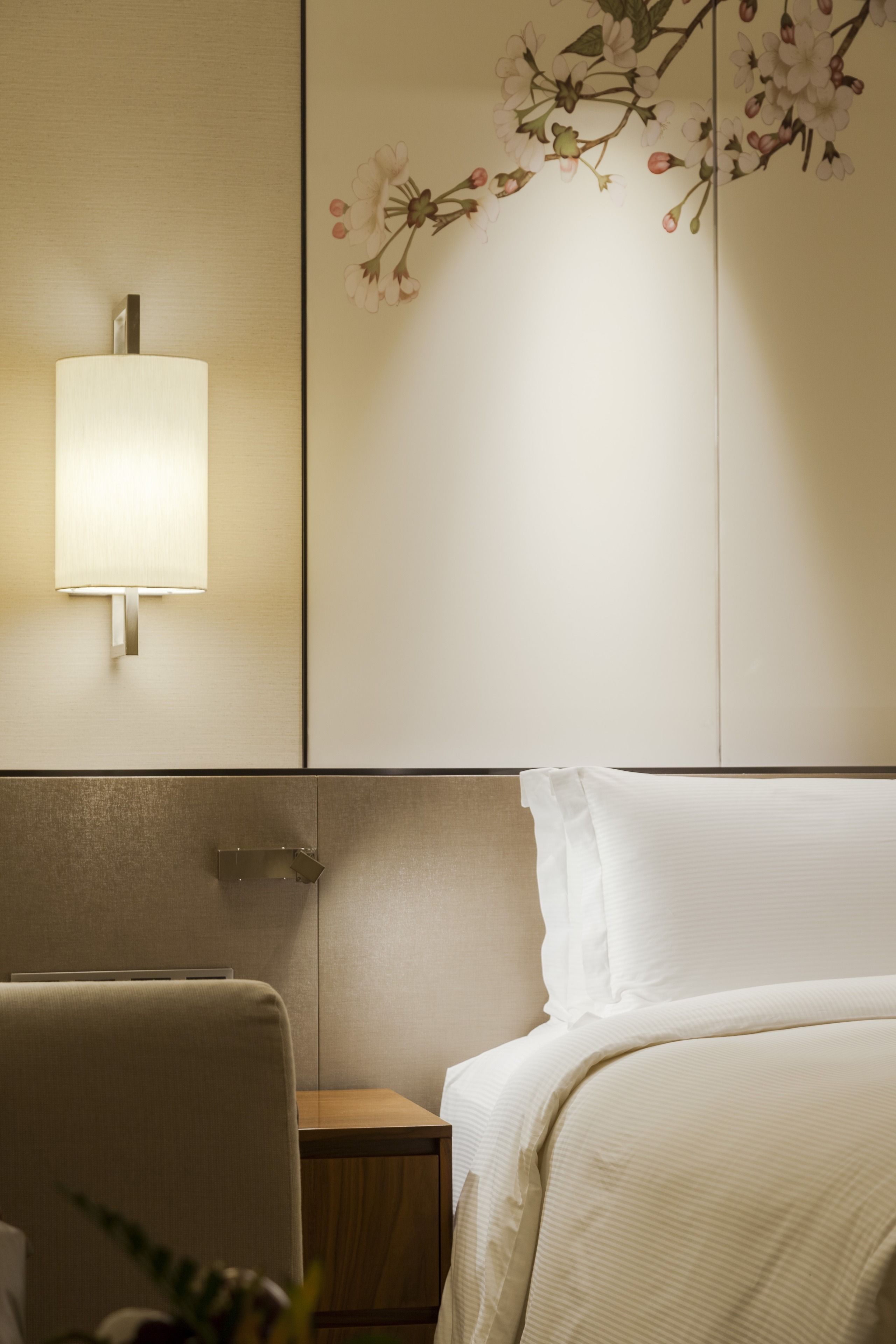 A hotel room with a bed, a nightstand, a lamp, and a wall with a floral design.