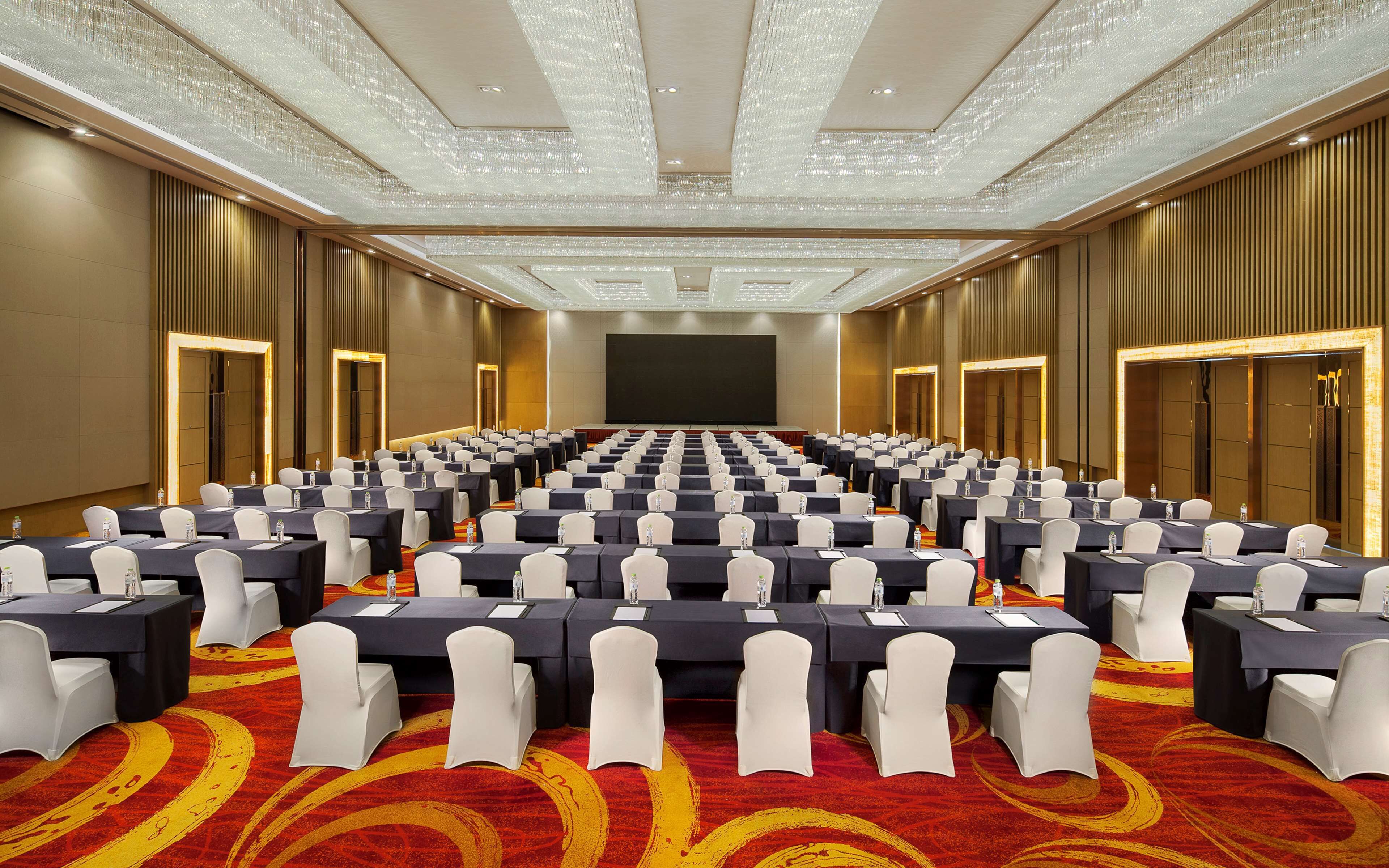 A conference room with rows of tables and chairs, a large screen, and a patterned carpet.