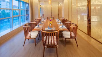 A conference room with a long table, wooden chairs, and a view through large windows.
