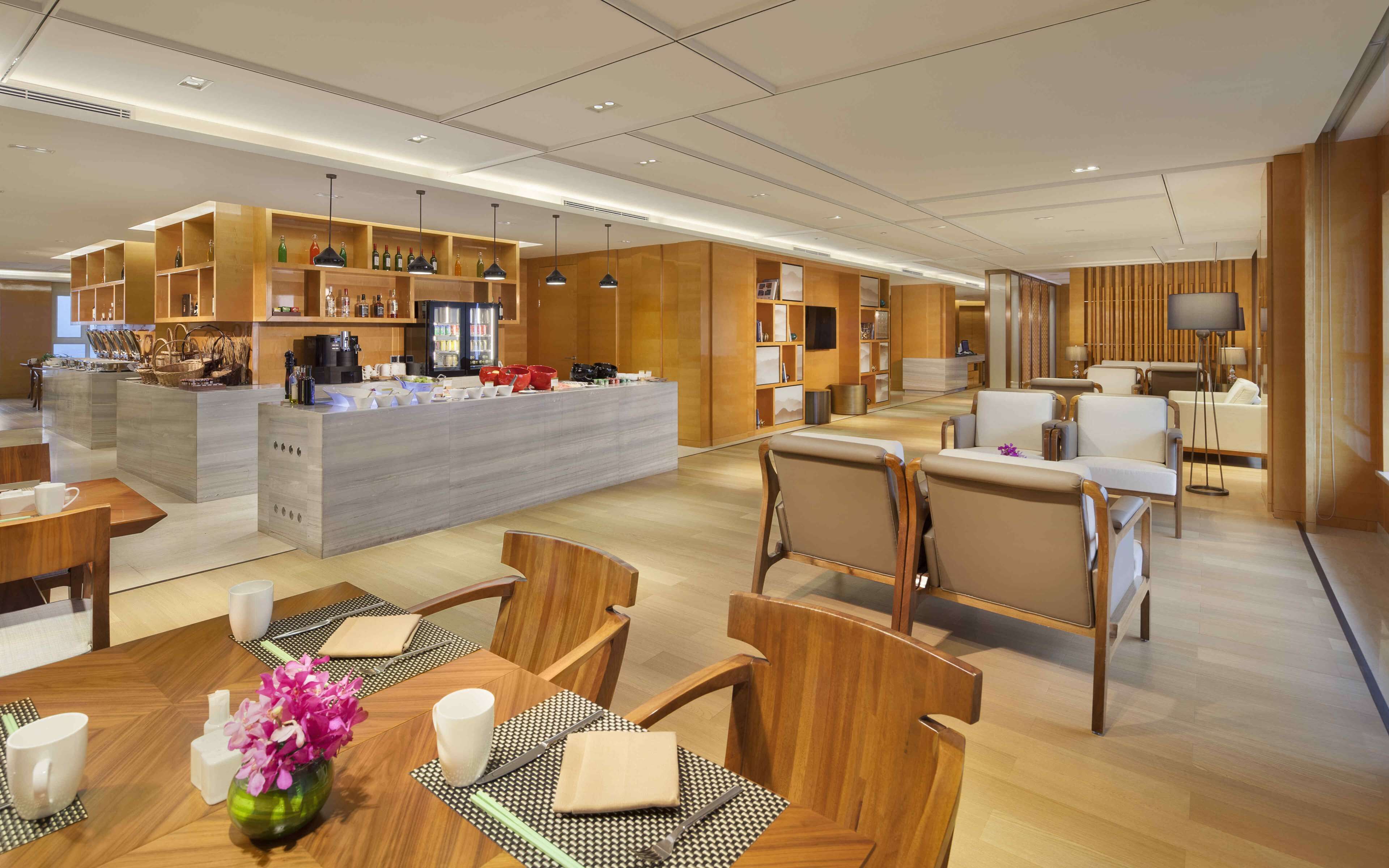 Un moderno vestíbulo de hotel con una zona de bar central, arreglos de asientos y una recepción.