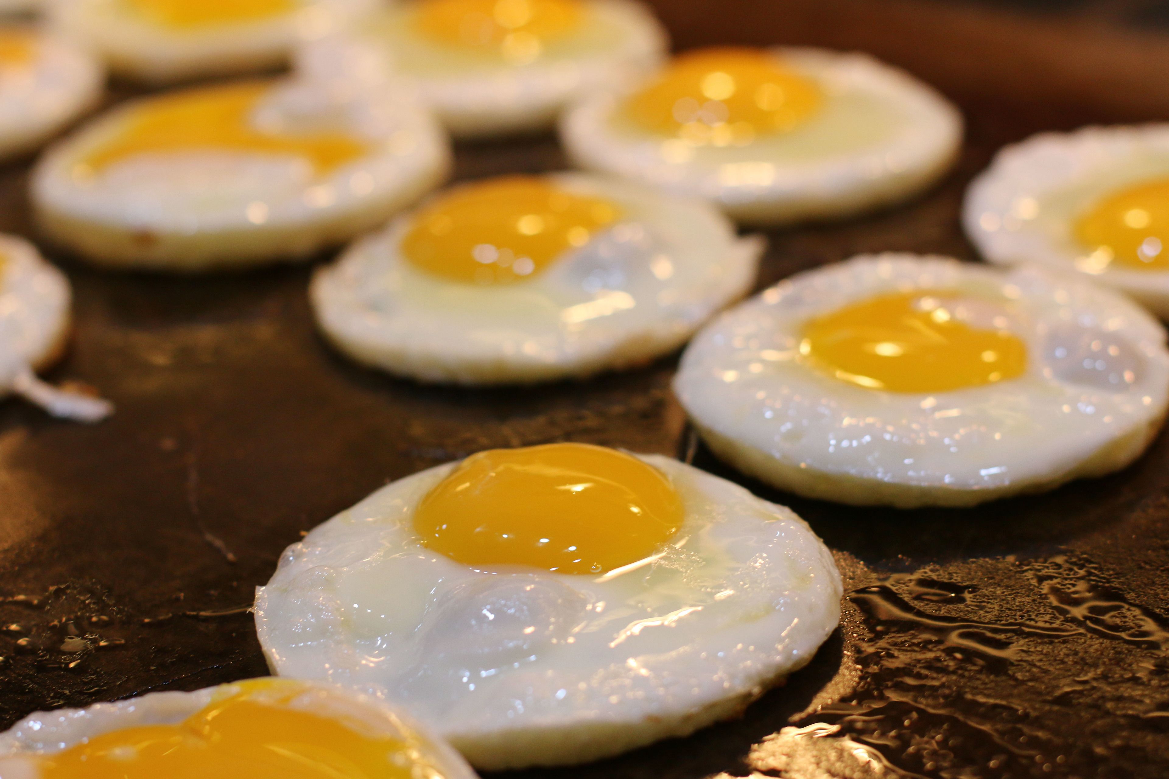 A close-up of several sunny-side-up eggs on a dark surface.