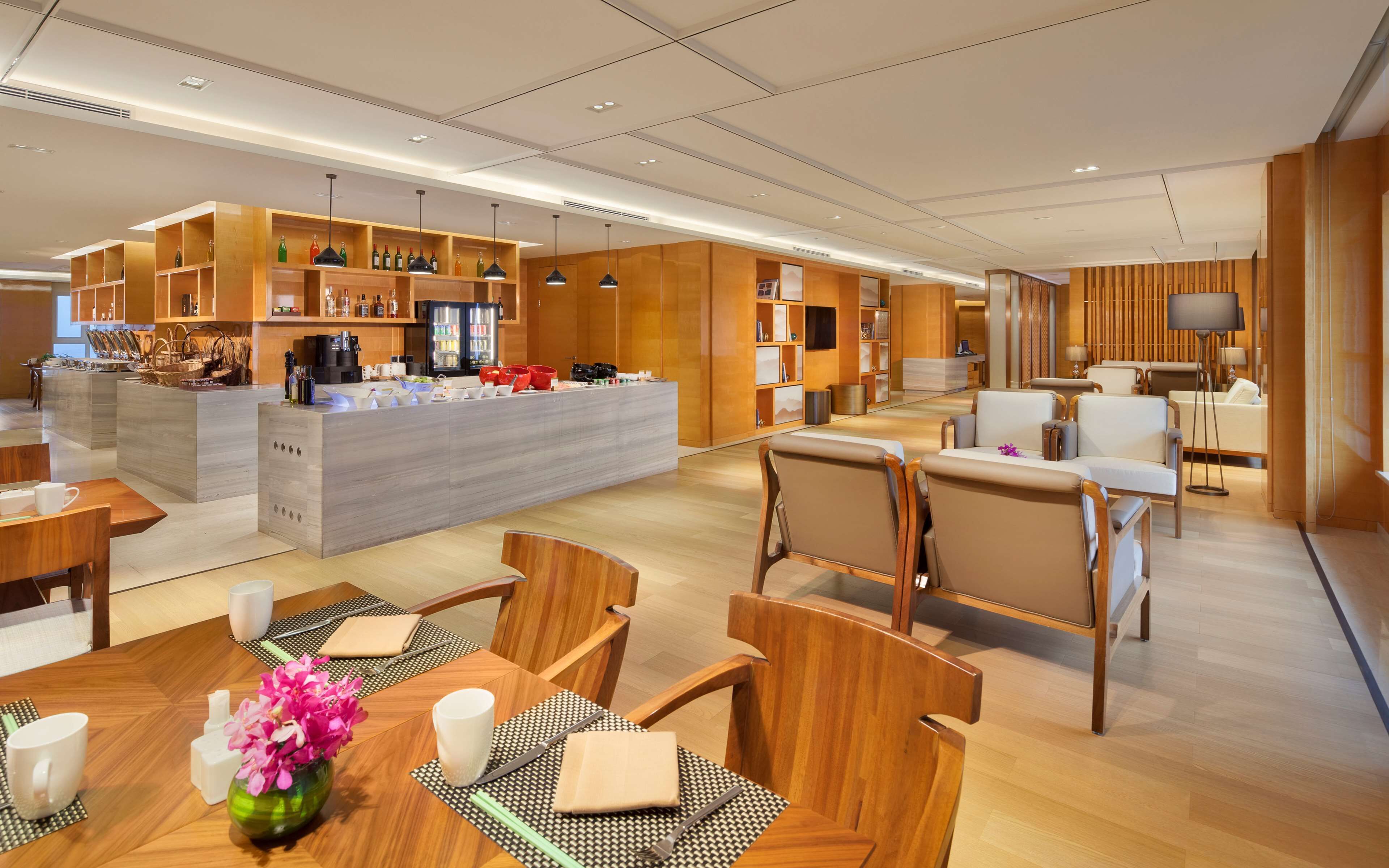 A modern hotel lobby with a central bar area, seating arrangements, and wooden decor.