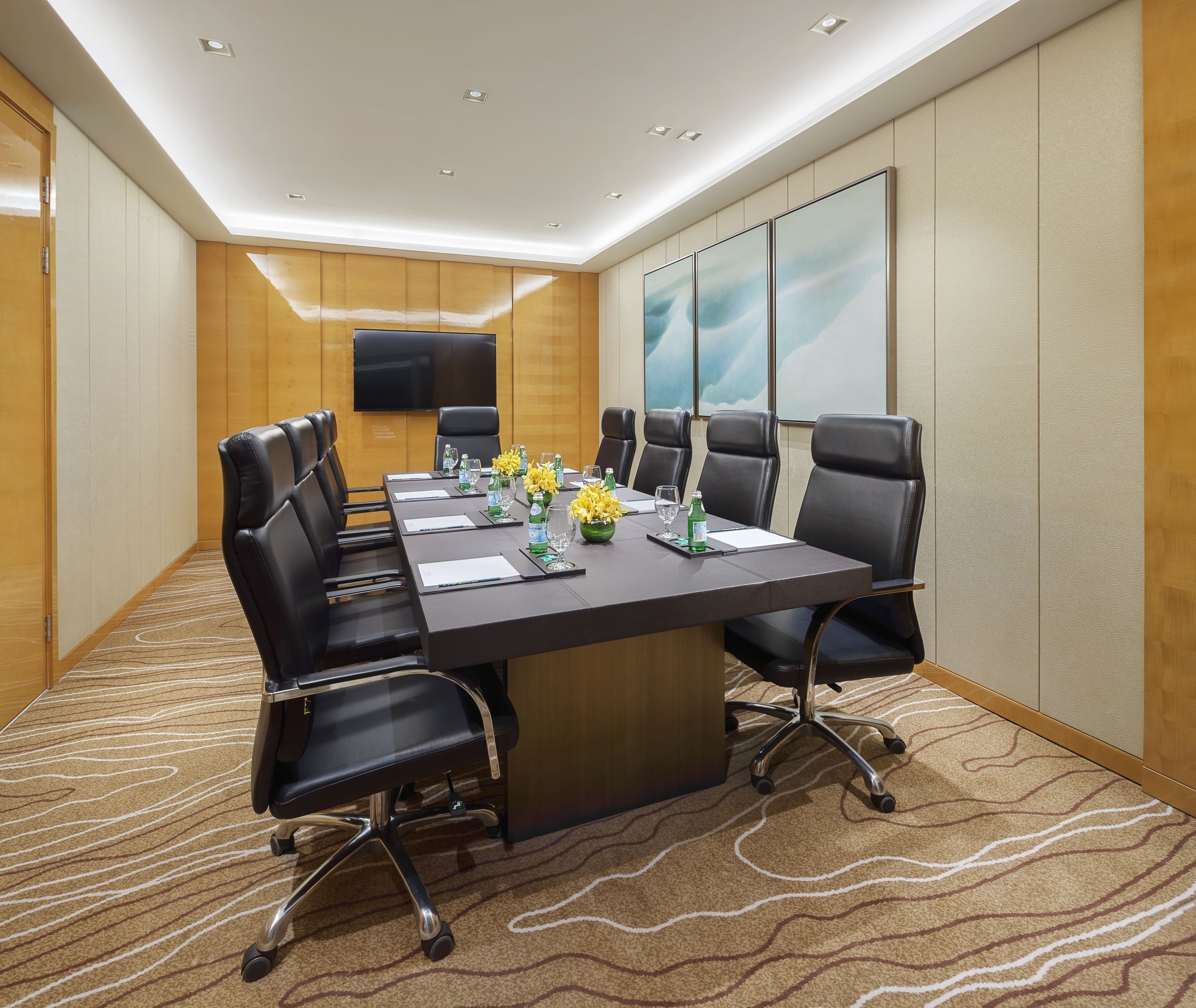 A conference room with a long table, black chairs, and a flat-screen TV on the wall.