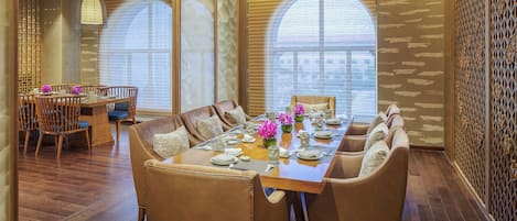 Un comedor con una larga mesa de madera, sillas acolchadas y un jarrón decorativo con flores.