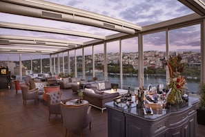 Un espacioso salón en la azotea con mobiliario moderno, una zona de bar y una vista panorámica de la ciudad.
