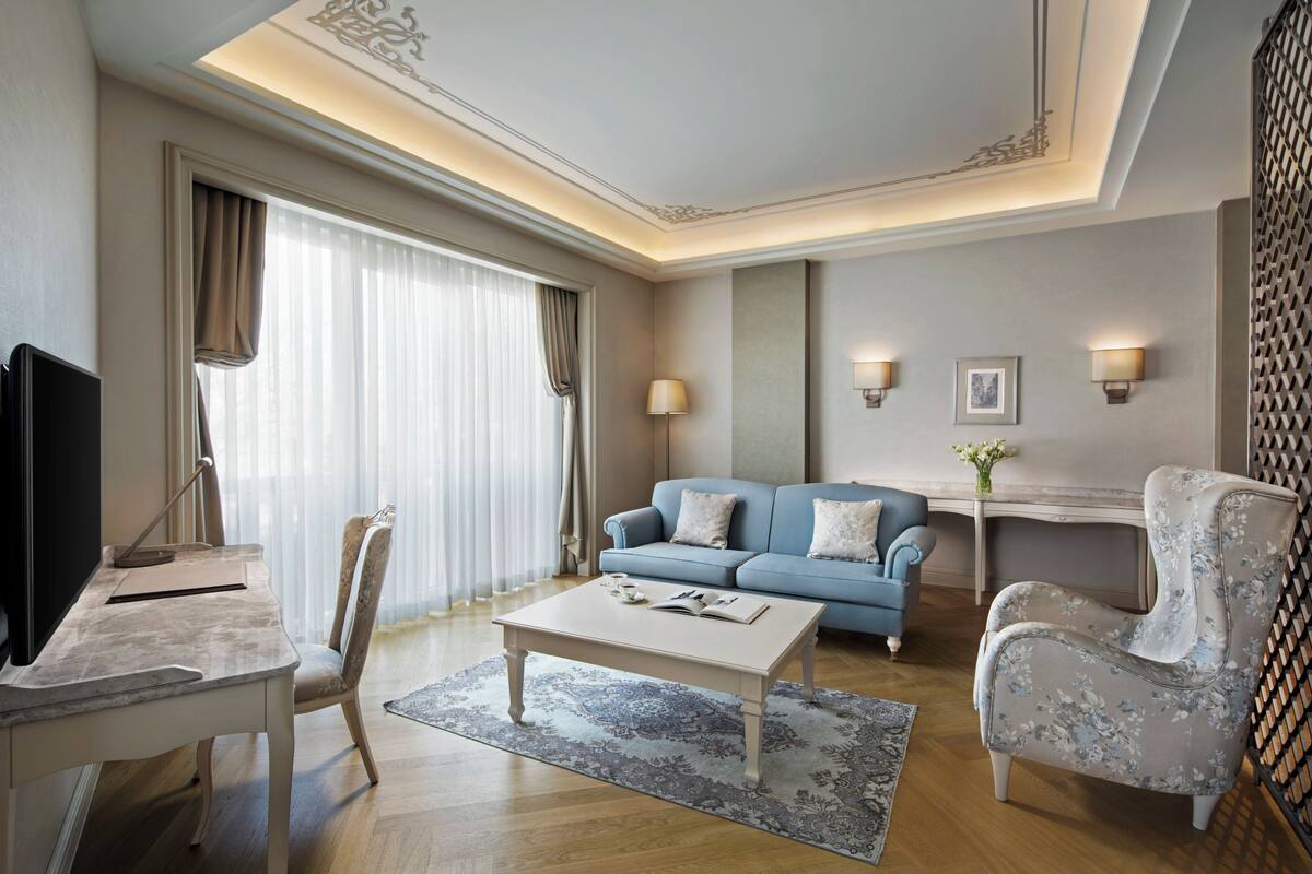 A hotel room with a flat-screen TV, a sofa, a coffee table, a chair, and a desk.