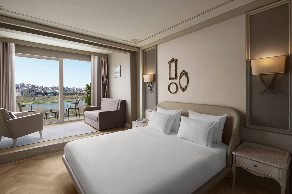 A hotel room with a large bed, a sofa, a desk, and a view of a cityscape.