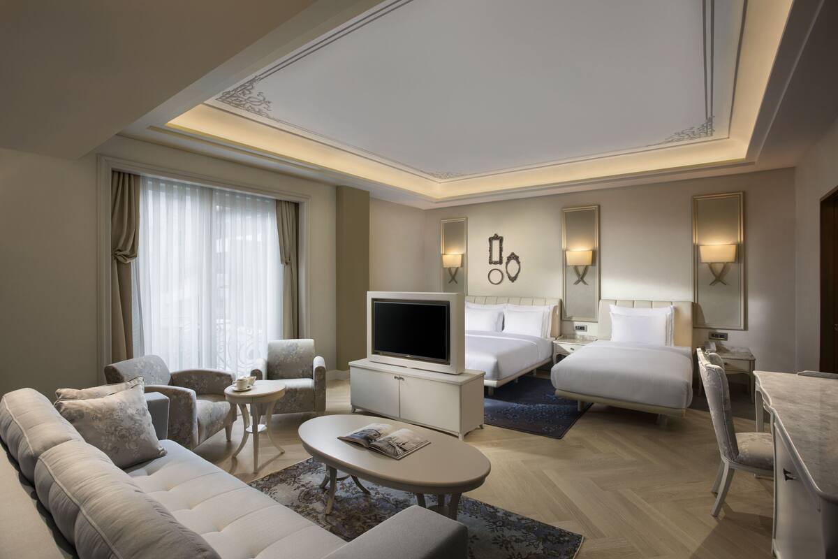 A hotel room with a sofa, a TV, a bed, a desk, and a chair.