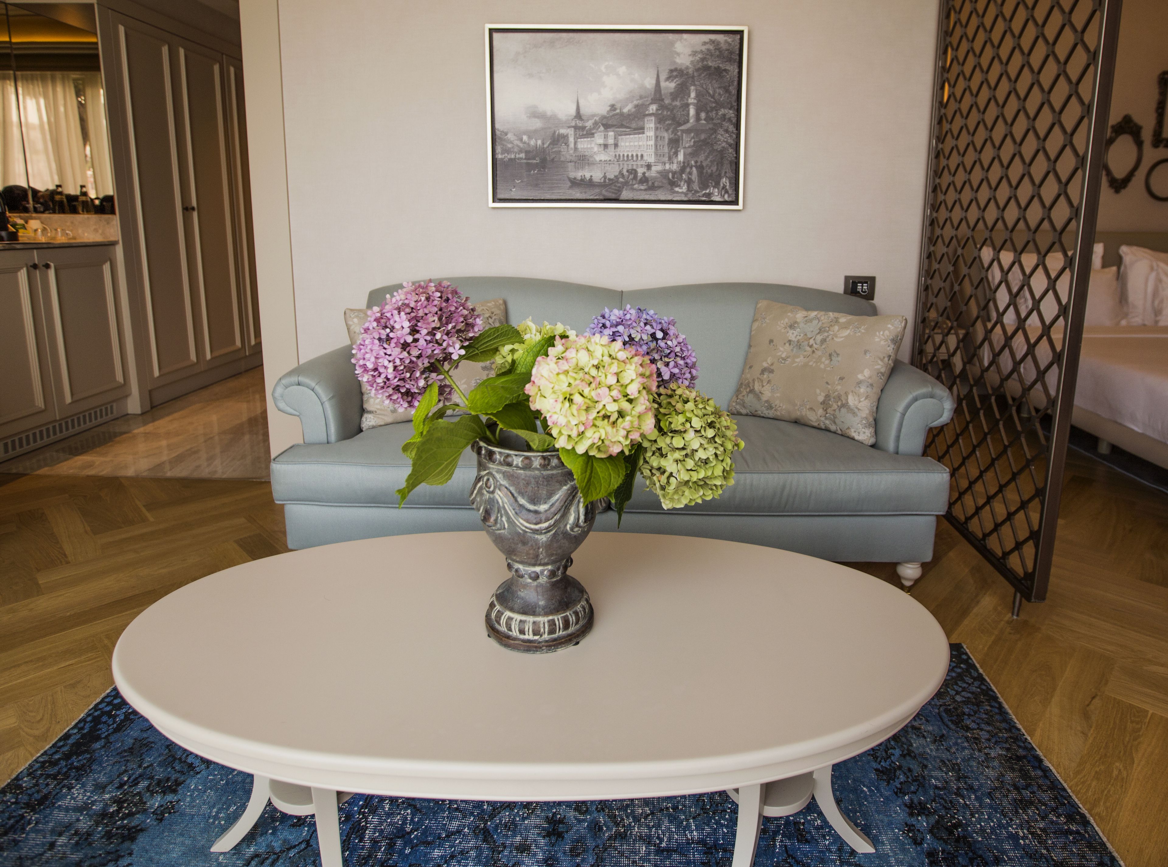 A living room with a round white table, a grey sofa, and a vase with flowers.
