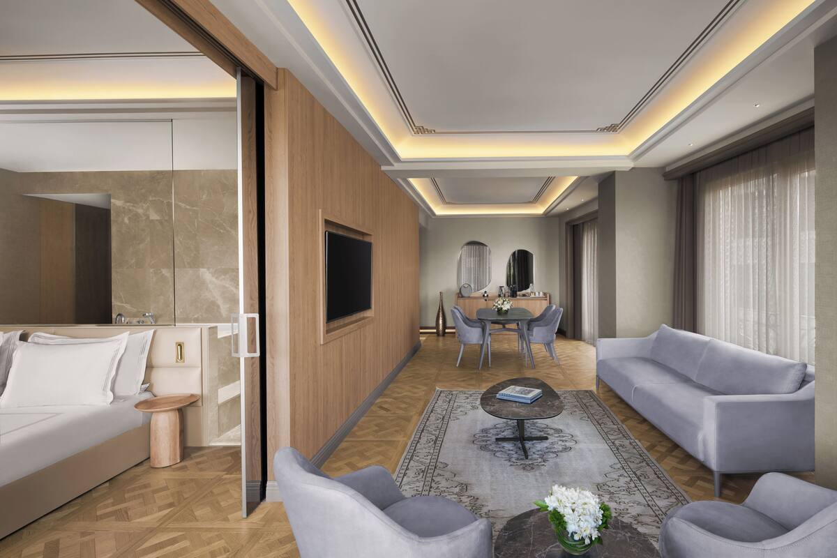 A modern hotel room with a bed, seating area, dining table, and a TV.