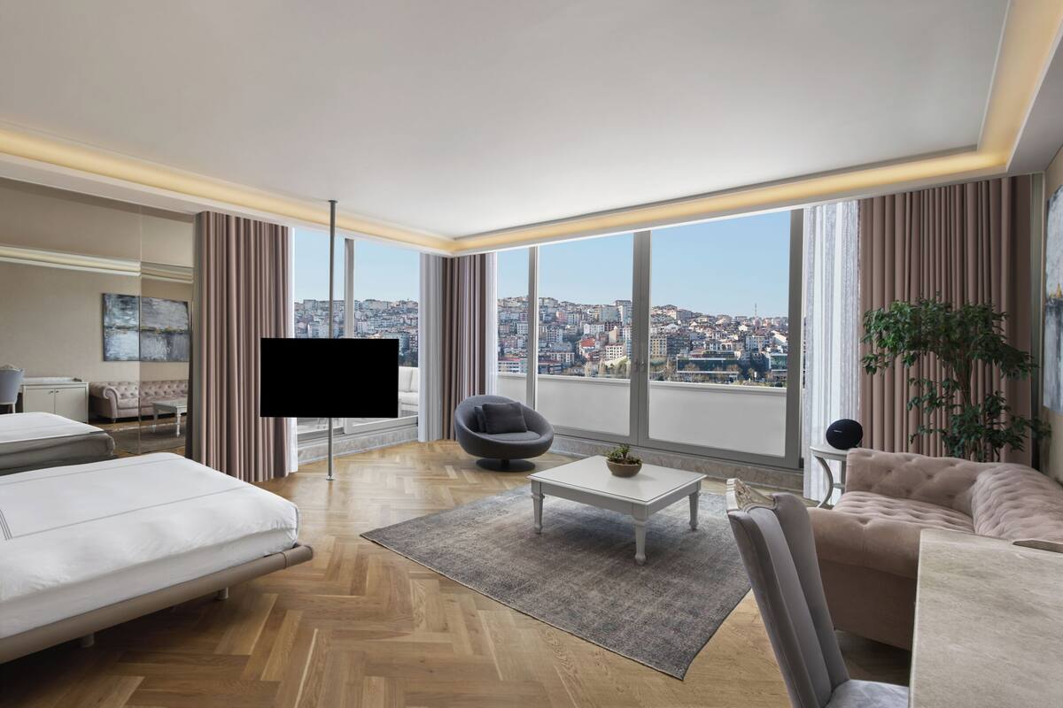 A modern hotel room with a bed, sofa, TV, and a city view.
