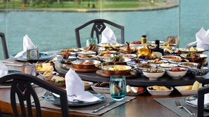 A table set with various dishes and drinks, overlooking a body of water. - Lazzoni Hotel (Istanbul)