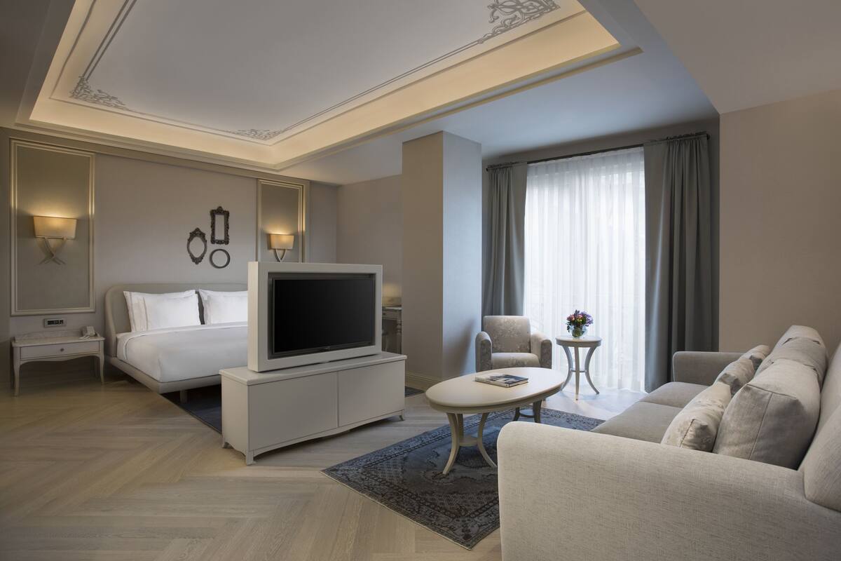 A hotel room with a bed, a TV, a sofa, and a small table.
