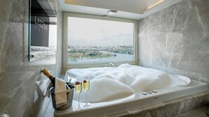 A luxurious bathroom with a large bathtub, a champagne bottle, and glasses, and a view of a cityscape through a large window. - Lazzoni Hotel (Istanbul)