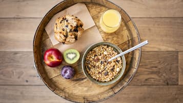 A wooden tray with a muffin, a bowl of granola, a glass of orange juice, and fresh fruits including an apple, kiwi, and plum.