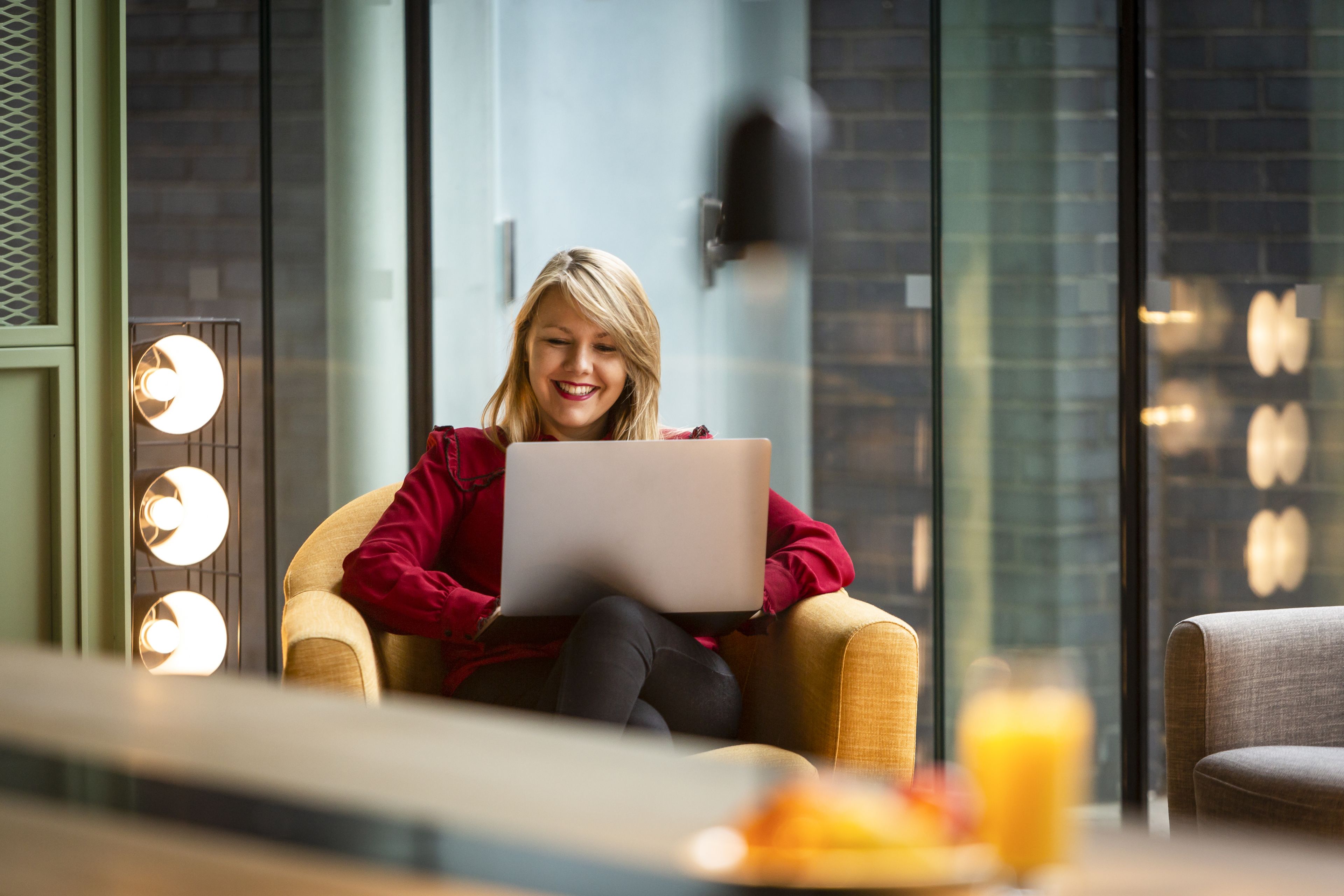 A person sitting on a chair with a laptop, in a room with a brick wall and a glass partition.