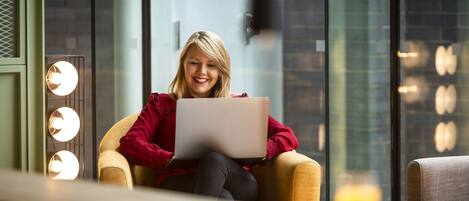 A person sitting on a chair with a laptop, in a room with a brick wall and a glass partition.