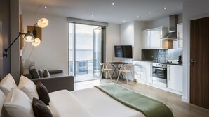 Een moderne hotelkamer met een groot bed, een balkon met uitzicht, een kitchenette en een flatscreen televisie.